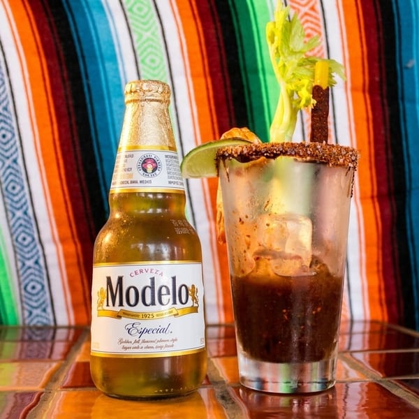 A Modelo Especial beer bottle next to a michelada with celery, lime, and a chili straw.