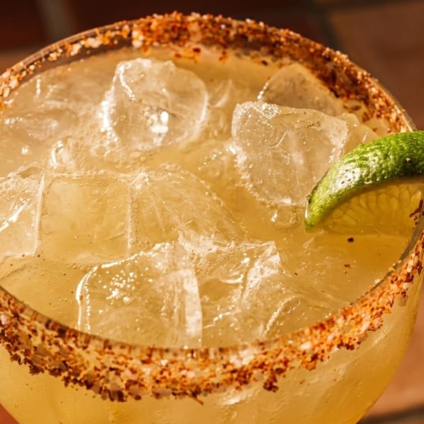 Close-up of a margarita with ice, a chili-salt rim, and a lime wedge.