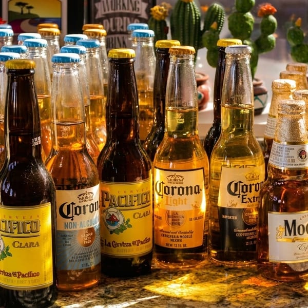 A variety of Mexican beer bottles, including Corona, Pacifico, and Modelo, on a sunlit counter.